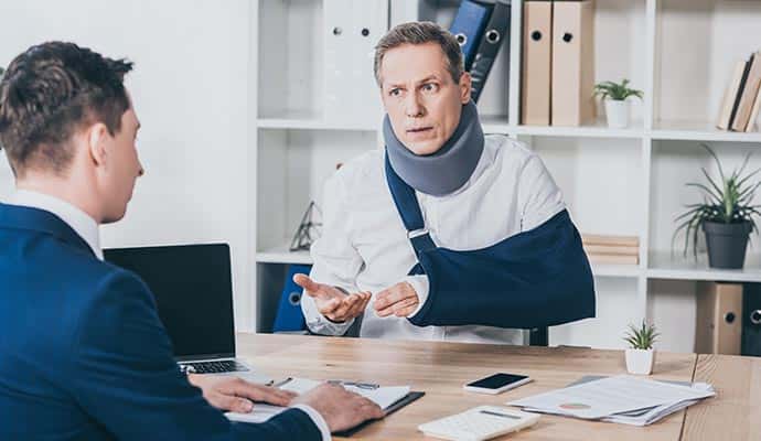 A man wearing a cervical neck brace and an arm sling sitting at a desk, discussing legal matter