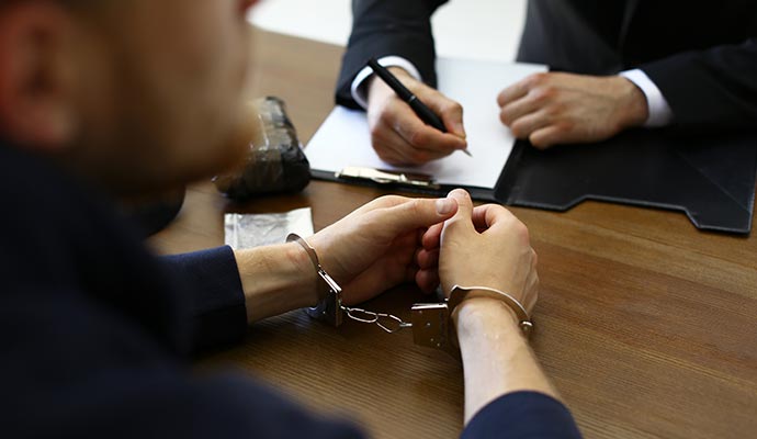 A person in handcuffs sitting at a wooden desk