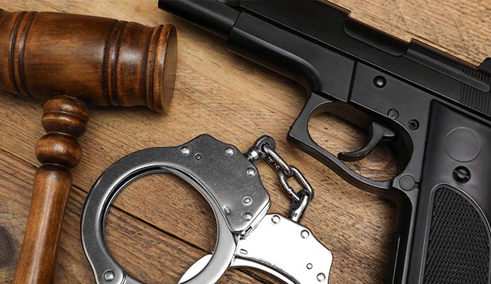 A wooden legal gavel, a pair of steel handcuffs, and a black handgun on wooden surface