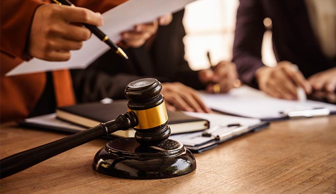 A wooden gavel on a desk and  several people are reviewing and signing documents