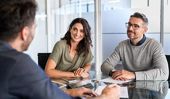 A smiling man and woman sitting at a glass conference table