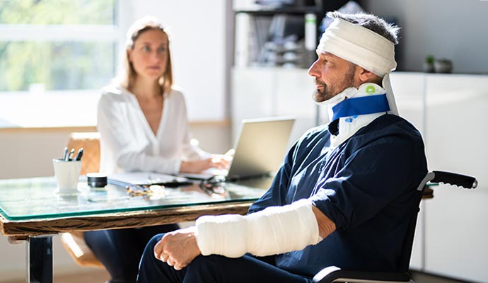 Injured man with head bandage neck brace and arm cast sitting in consultation